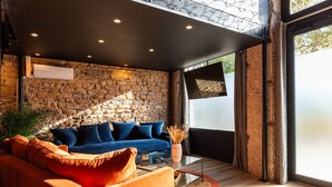 A modern living room with a stone wall, blue sofa, orange armchair, and a glass coffee table.
