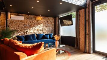 Un salon moderne avec un mur en pierre, un canapé bleu, un fauteuil orange et une table basse en verre.