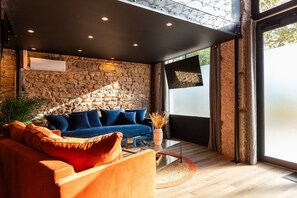 Un salon moderne avec un mur en pierre, un canapé bleu, un fauteuil orange et une table basse en verre.