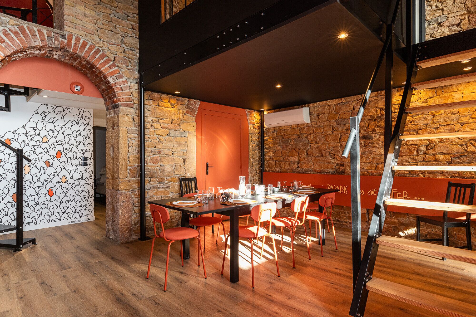 Un restaurant avec un mur en pierre rustique, un plancher en bois et des chaises rouges.