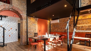A restaurant with a rustic stone wall, wooden flooring, and red chairs.