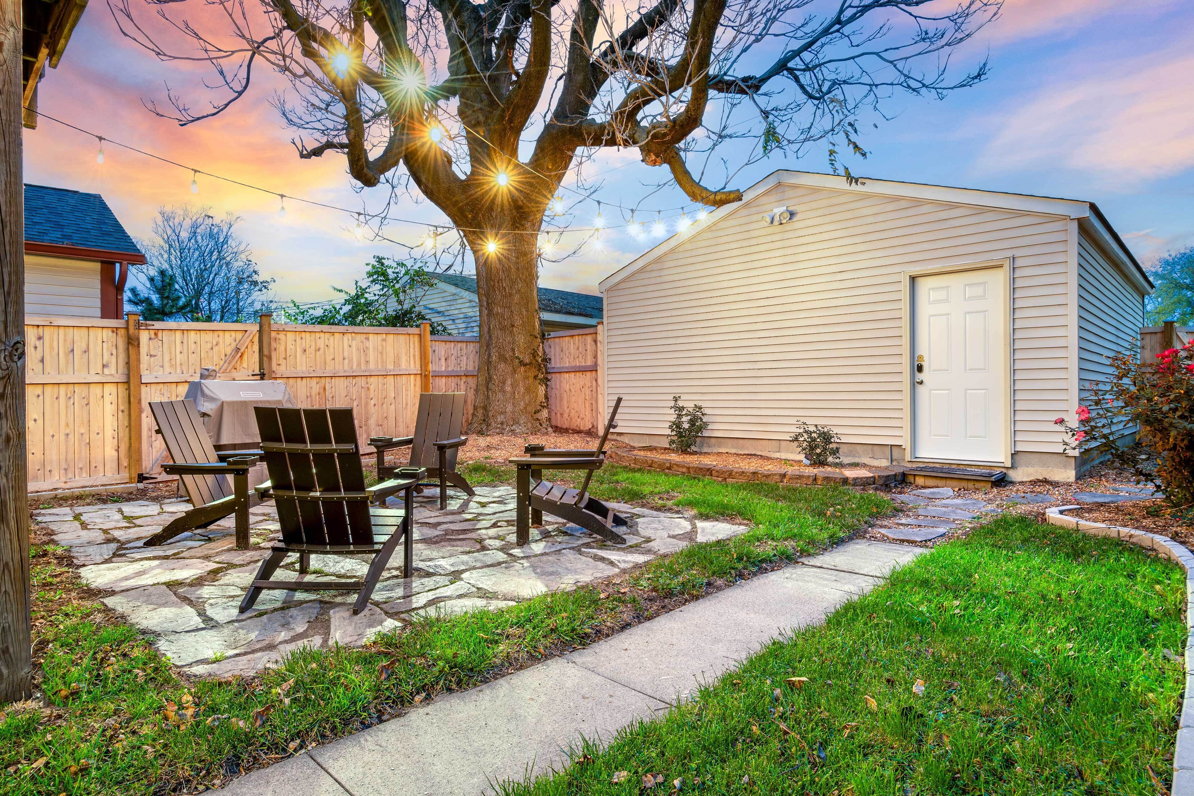 A backyard with a stone patio, wooden chairs, and a barbecue grill.