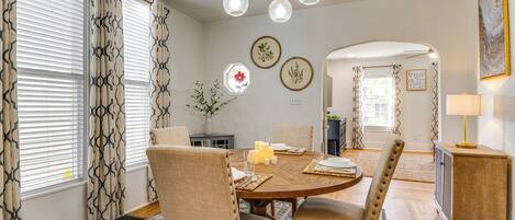 A dining area with a round wooden table, beige upholstered chairs, and a chandelier.