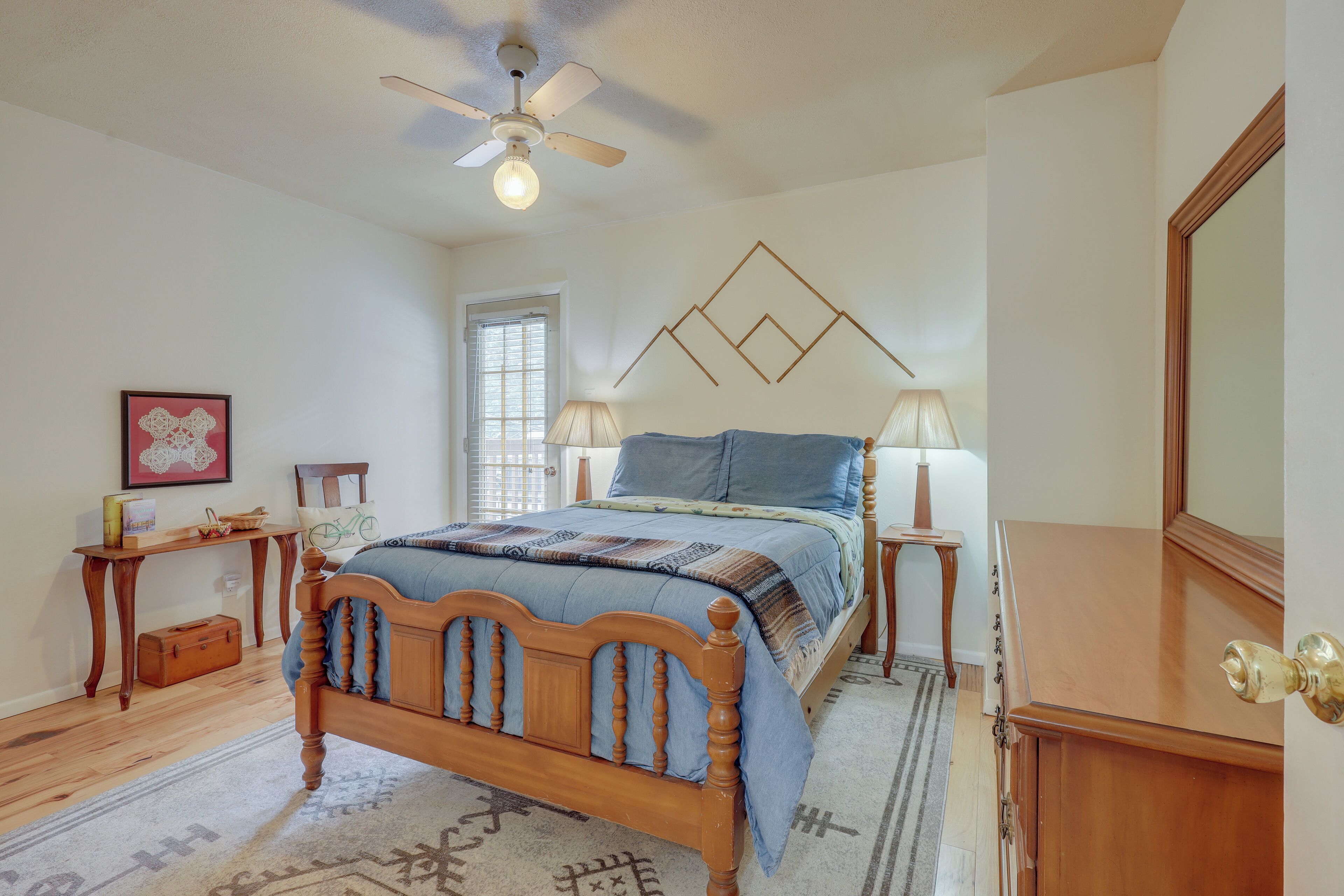 A bedroom with a wooden bed, a ceiling fan, a window, and a nightstand with a lamp.