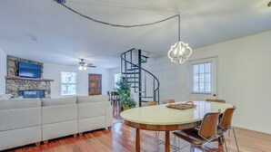A spacious living room with a large sofa, a dining table with chairs, a spiral staircase, and a TV mounted on a stone wall. - Mountainside Bliss: Red River Getaway w/ Fireplace (Red River)