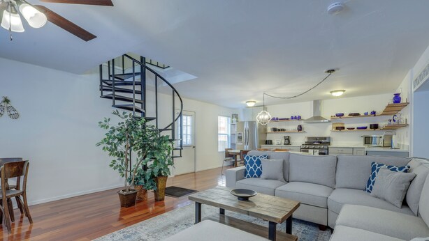 A modern living room with a wooden floor, a grey sofa, a coffee table, and a spiral staircase leading to an upper level. - Mountainside Bliss: Red River Getaway w/ Fireplace (Red River)