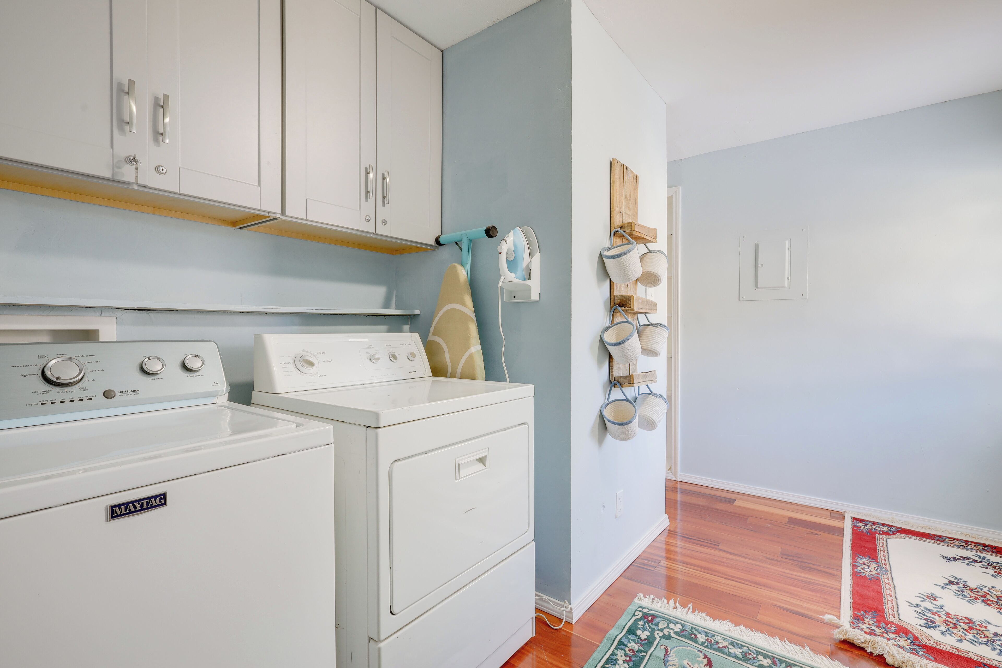 A laundry area with a Maytag washer and dryer, wooden shelves, and a hanging rack with cups.