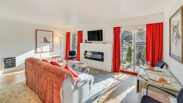 A modern living room with a sofa, a flat-screen TV, a fireplace, and a dining area with a table set for two. - Ketchum Vacation Rental - Hike, Ski & Explore! (Ketchum)