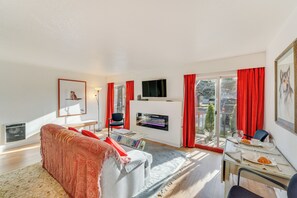 A modern living room with a sofa, a flat-screen TV, a fireplace, and a dining area with a table set for two.