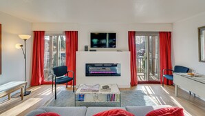 A modern living room with a fireplace, a flat-screen TV, and a dining area with red curtains. - Ketchum Vacation Rental - Hike, Ski & Explore! (Ketchum)