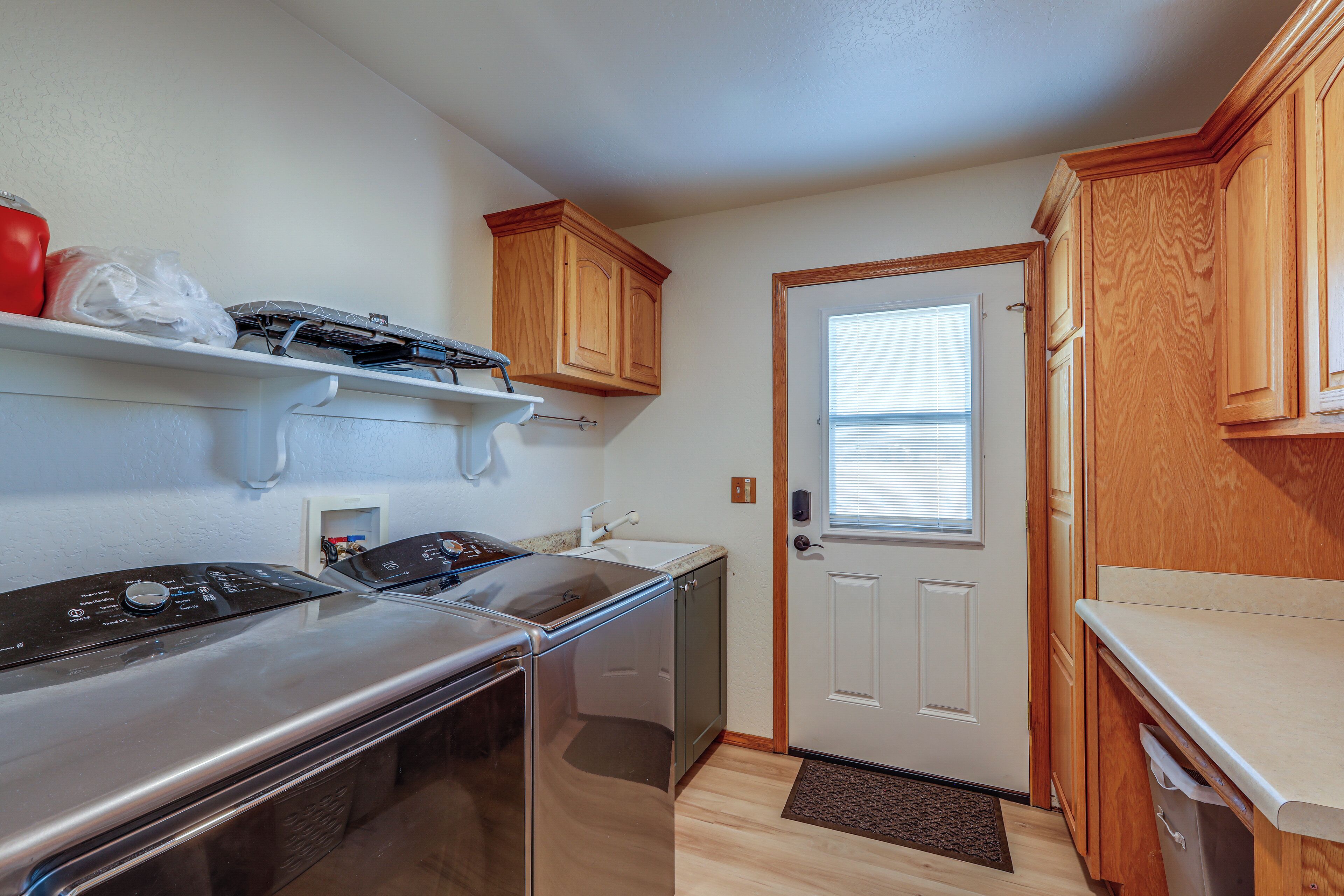 A compact kitchen with a stainless steel washer, a dishwasher, wooden cabinets, and a white door with a window.