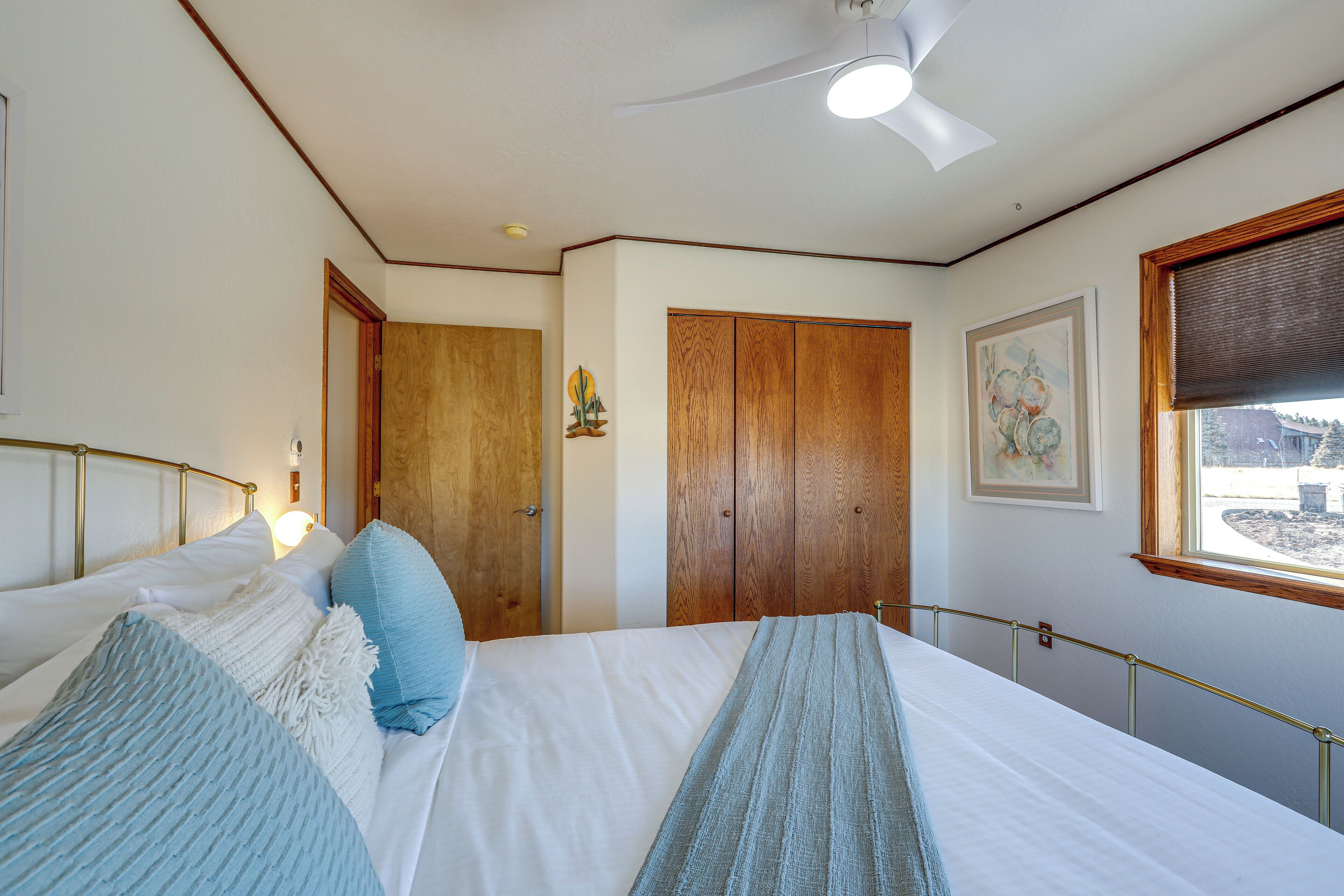 A bedroom with a bed, two doors, a ceiling fan, and a window with a view.