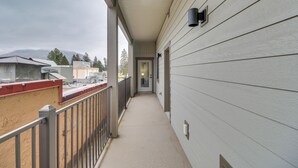 A narrow balcony with a metal railing, a door at the end, and a view of buildings and mountains in the background. - Downtown Columbia Falls Condo: 16 Mi to Ski Resort (Columbia Falls)