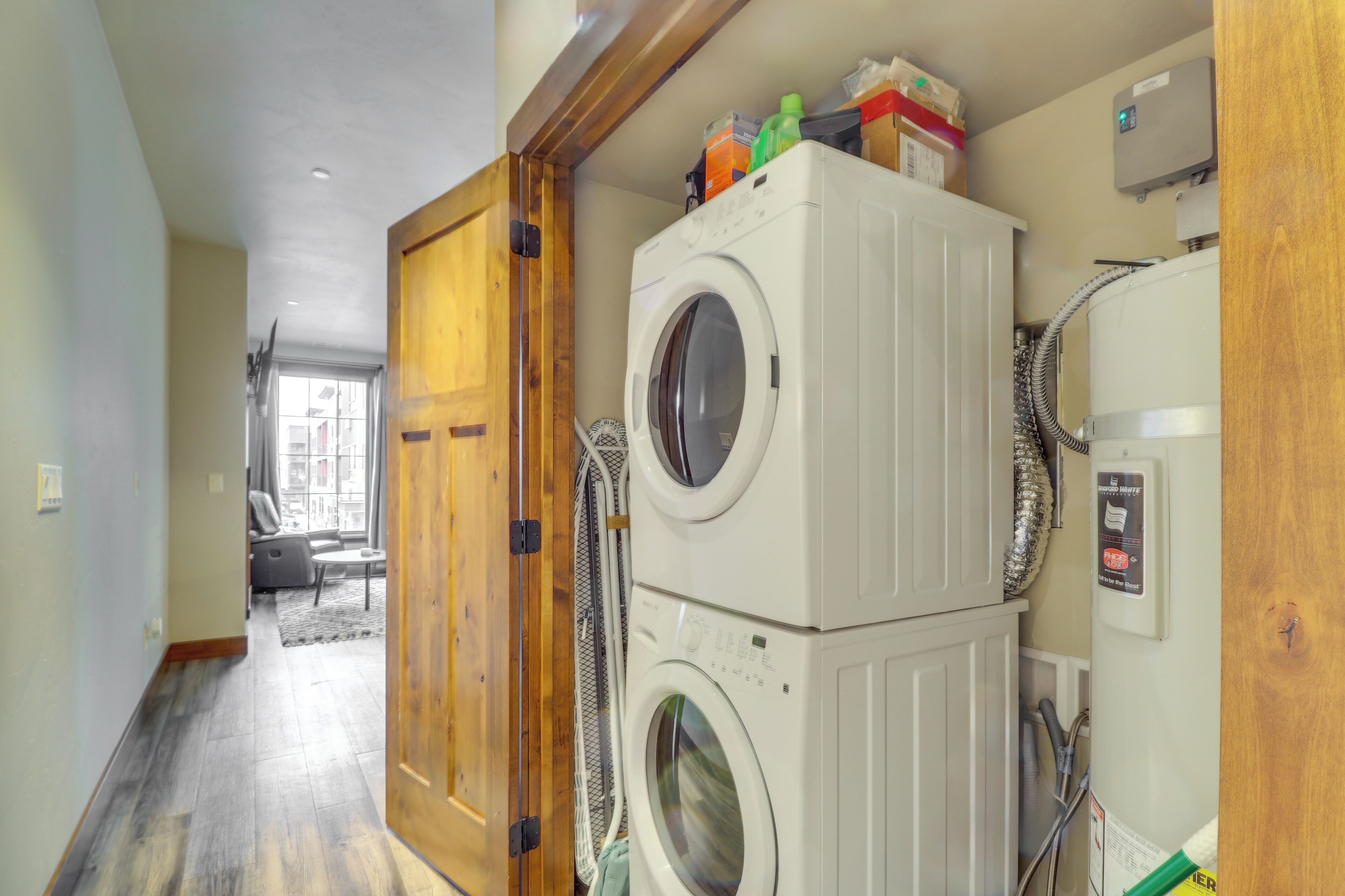 A laundry room with stacked washers and dryers, a wooden door, and a window in the background.