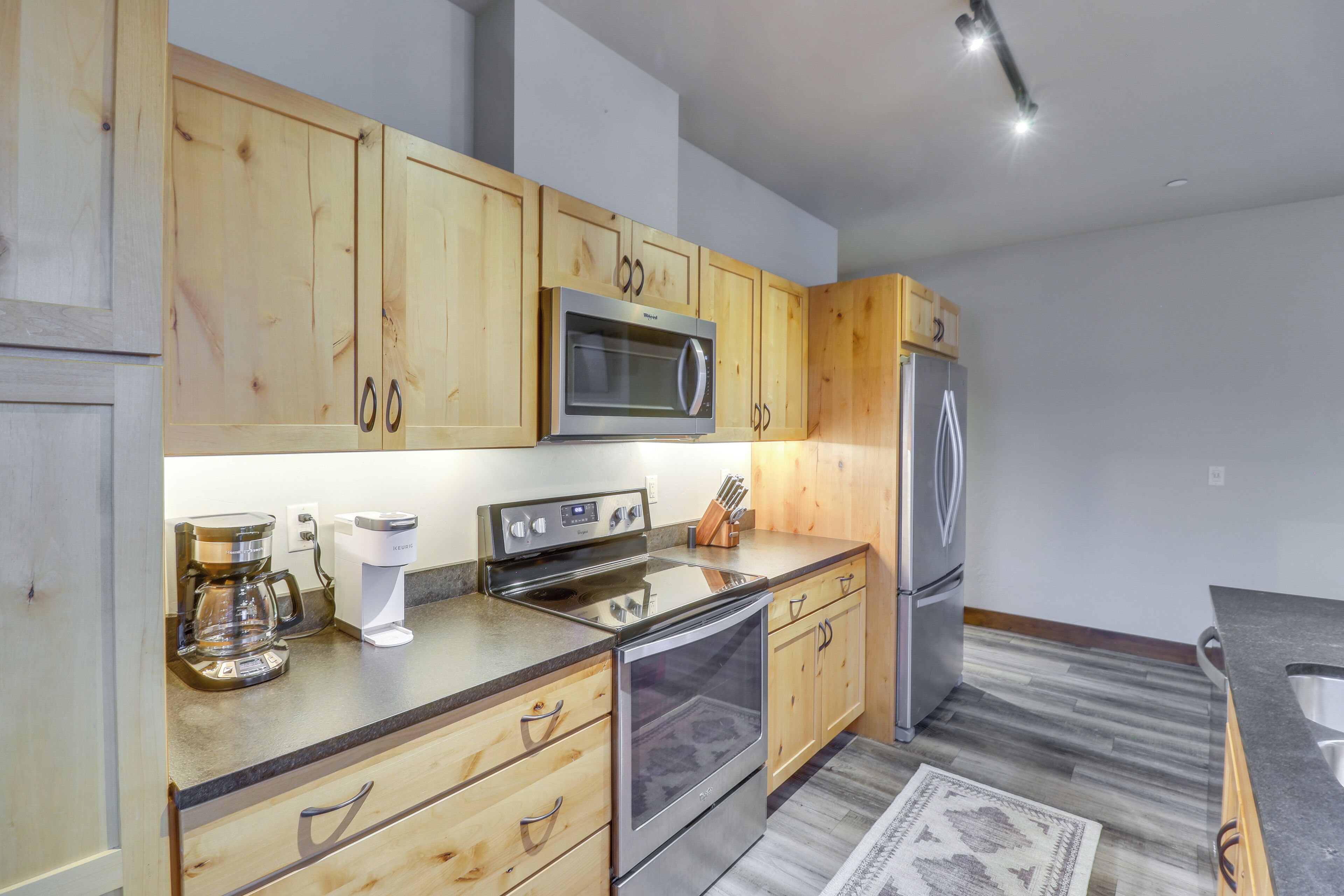 A modern kitchen with wooden cabinets, stainless steel appliances, and a coffee maker.