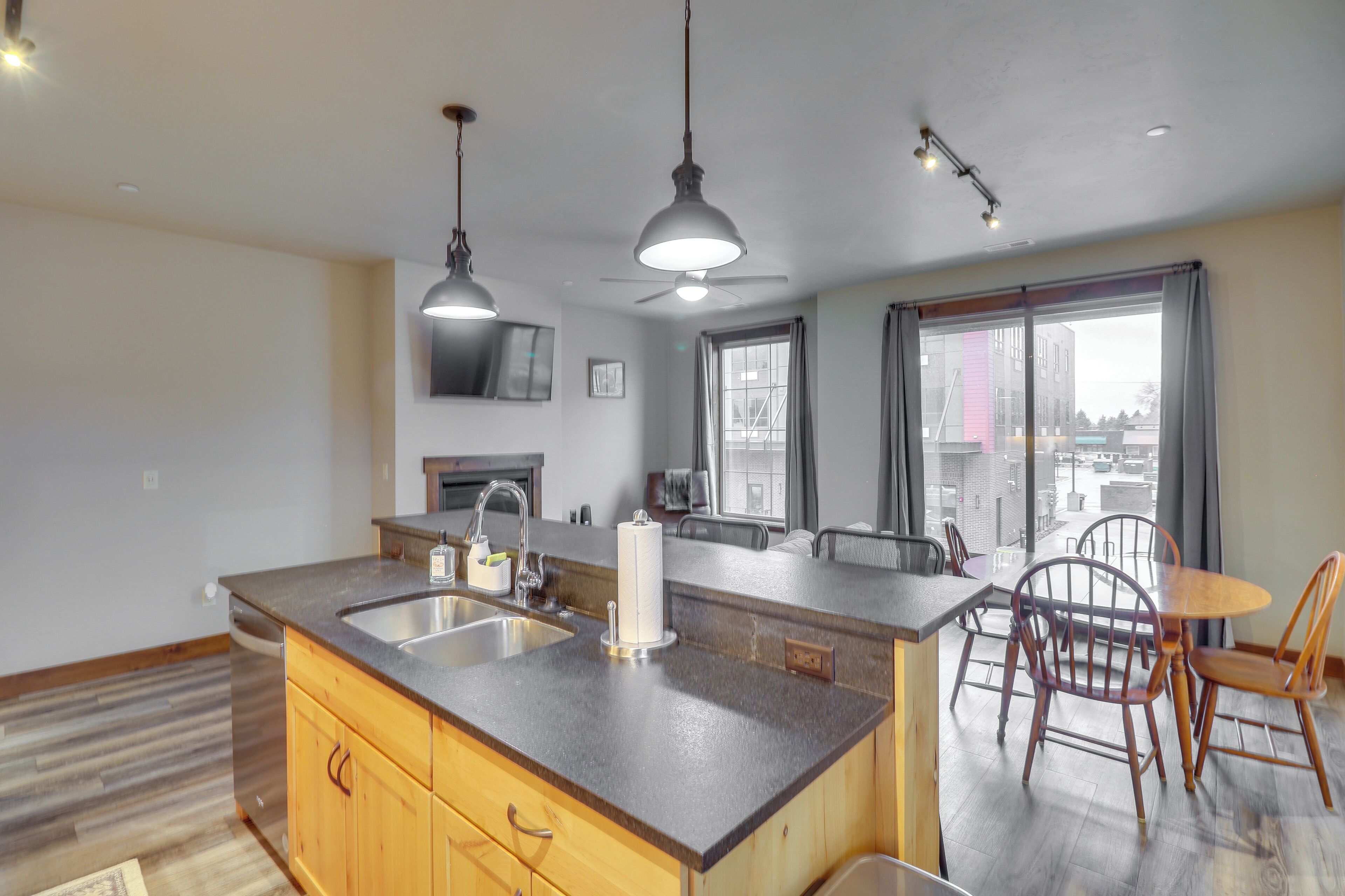 Una cocina con una isla central, un comedor con sillas, un ventilador de techo y un amplio ventanal con cortinas.