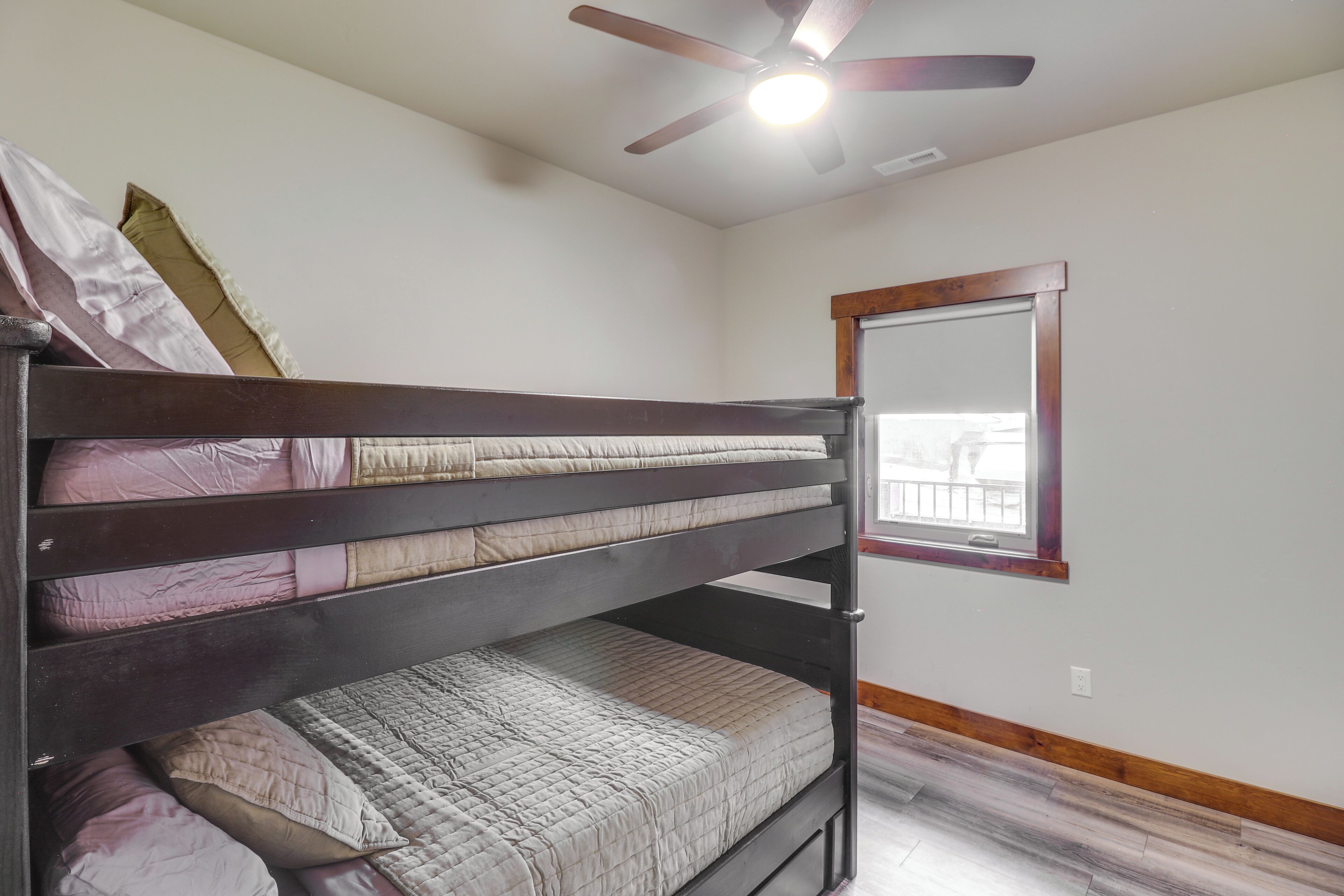 A bunk bed with a ceiling fan, a window with a wooden frame, and a white wall.