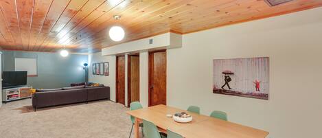A room with a wooden ceiling, a dining table with chairs, a sofa, and a television.
