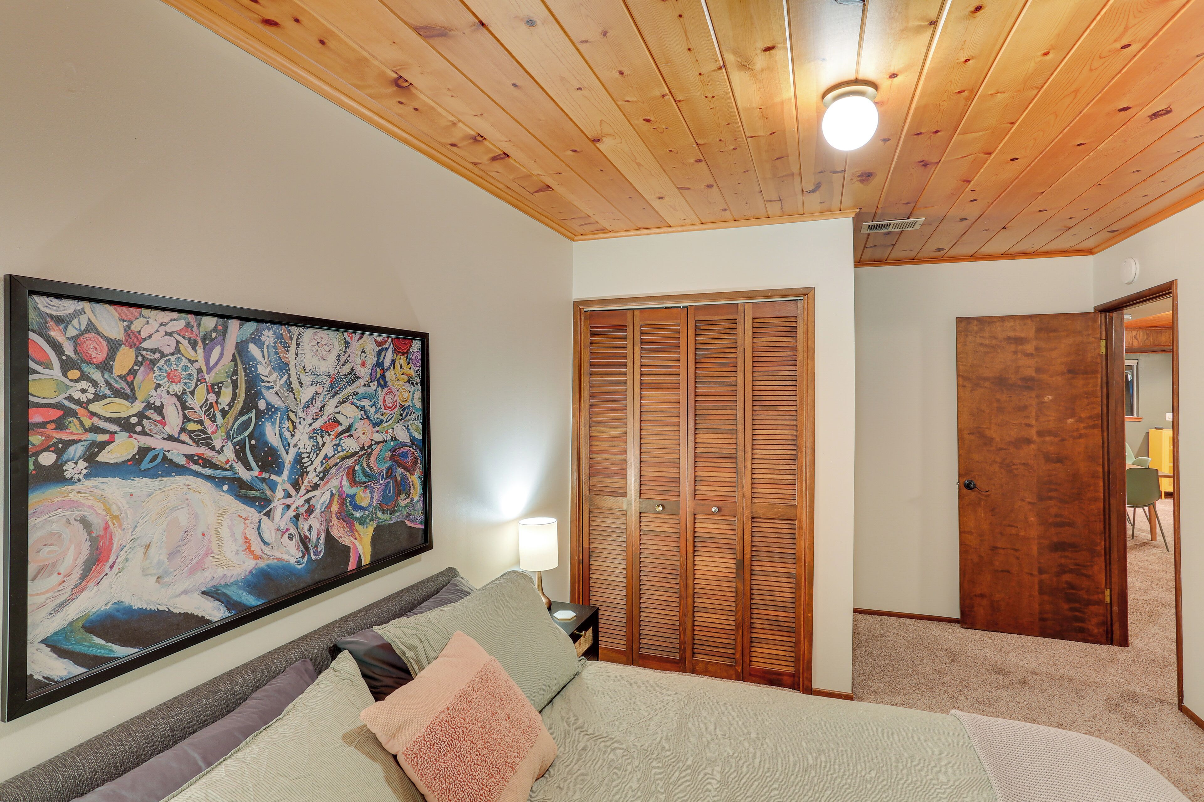 Une chambre à coucher avec un grand tableau abstrait, un lit avec de nombreux coussins, des armoires en bois et un luminaire au plafond.