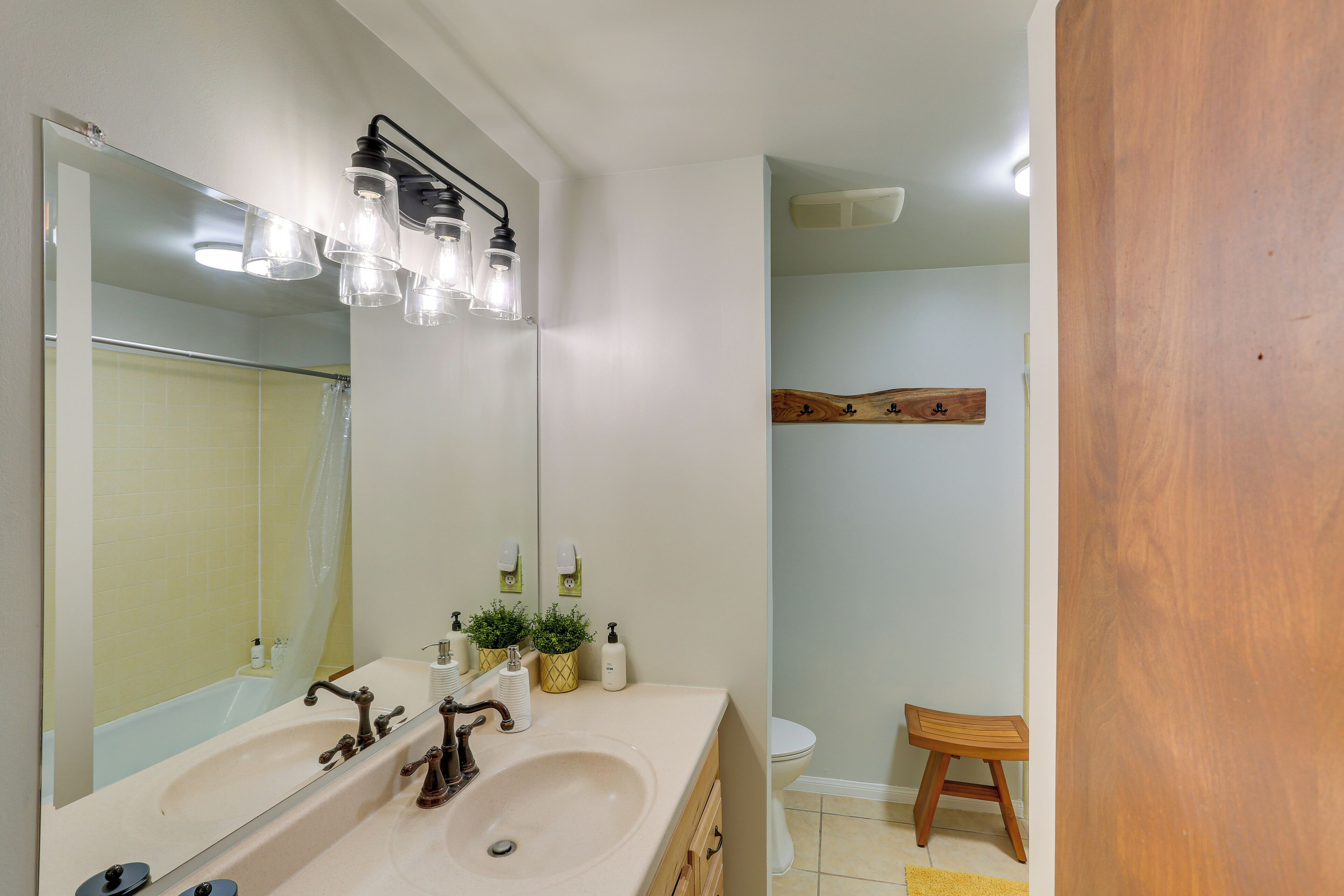 A bathroom with a double sink, a large mirror, and a wooden shelf.