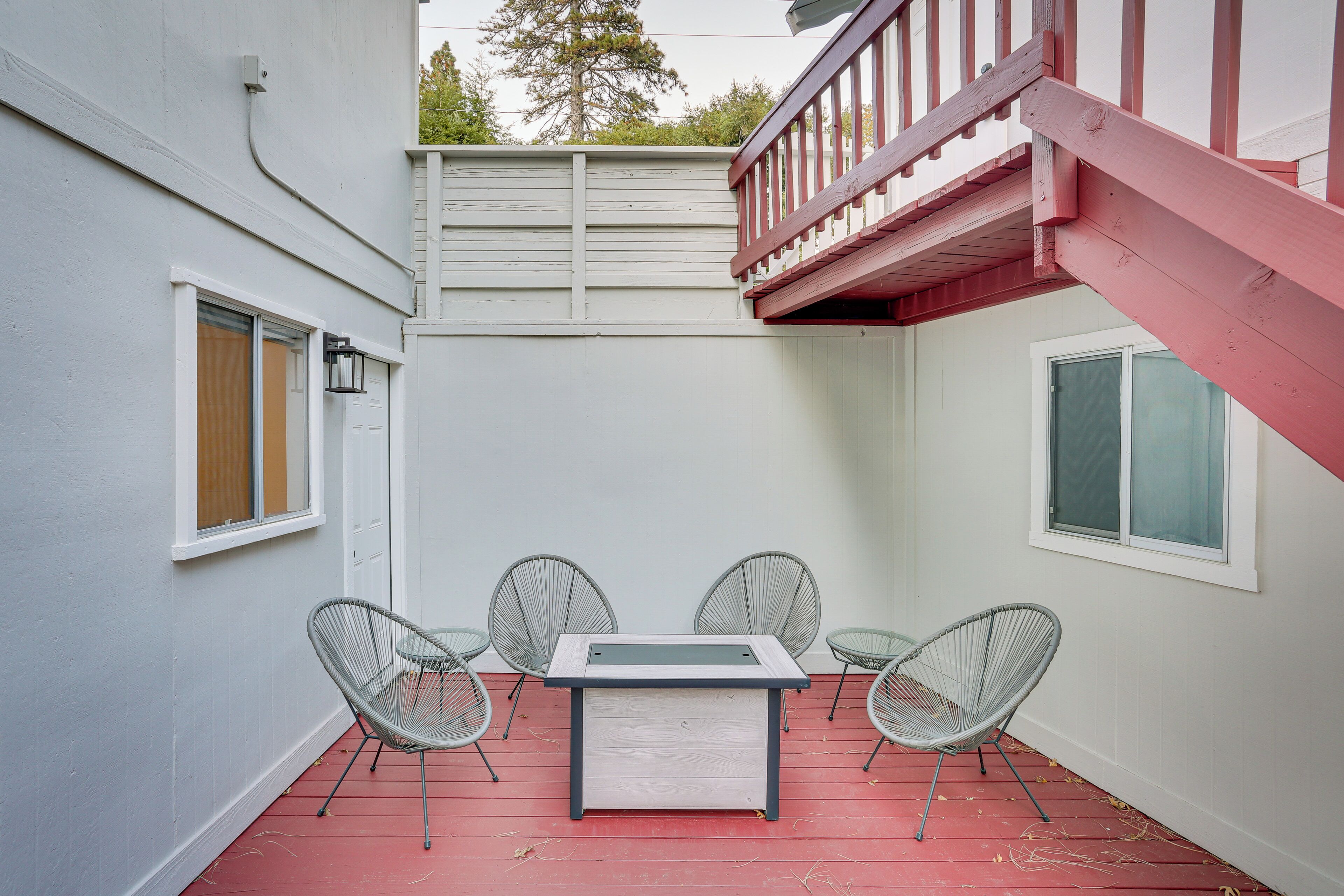A small outdoor patio with a table and four chairs, a red staircase, and a white wall.