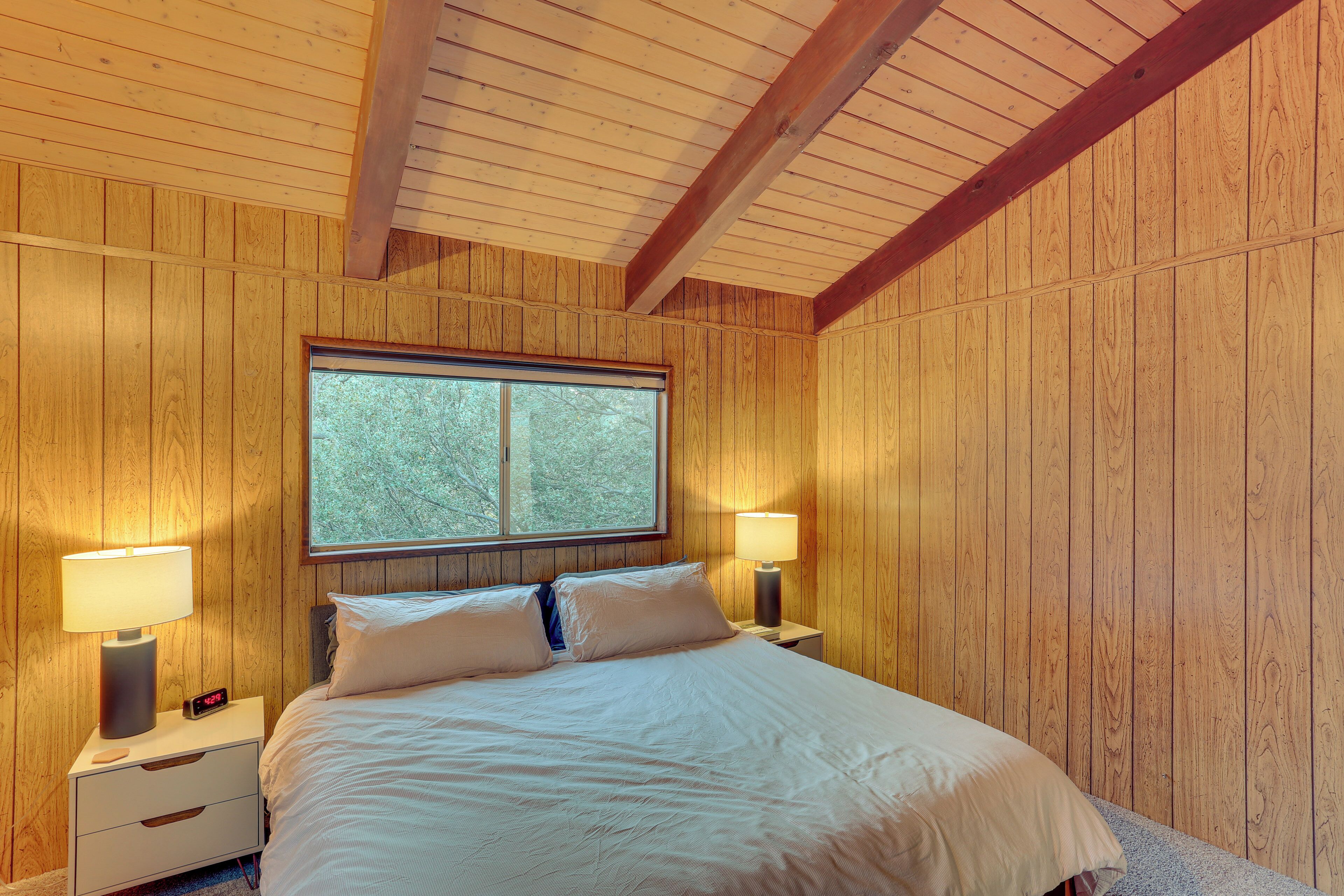 A wooden-paneled bedroom with a bed, two bedside tables, a nightstand, and a window.