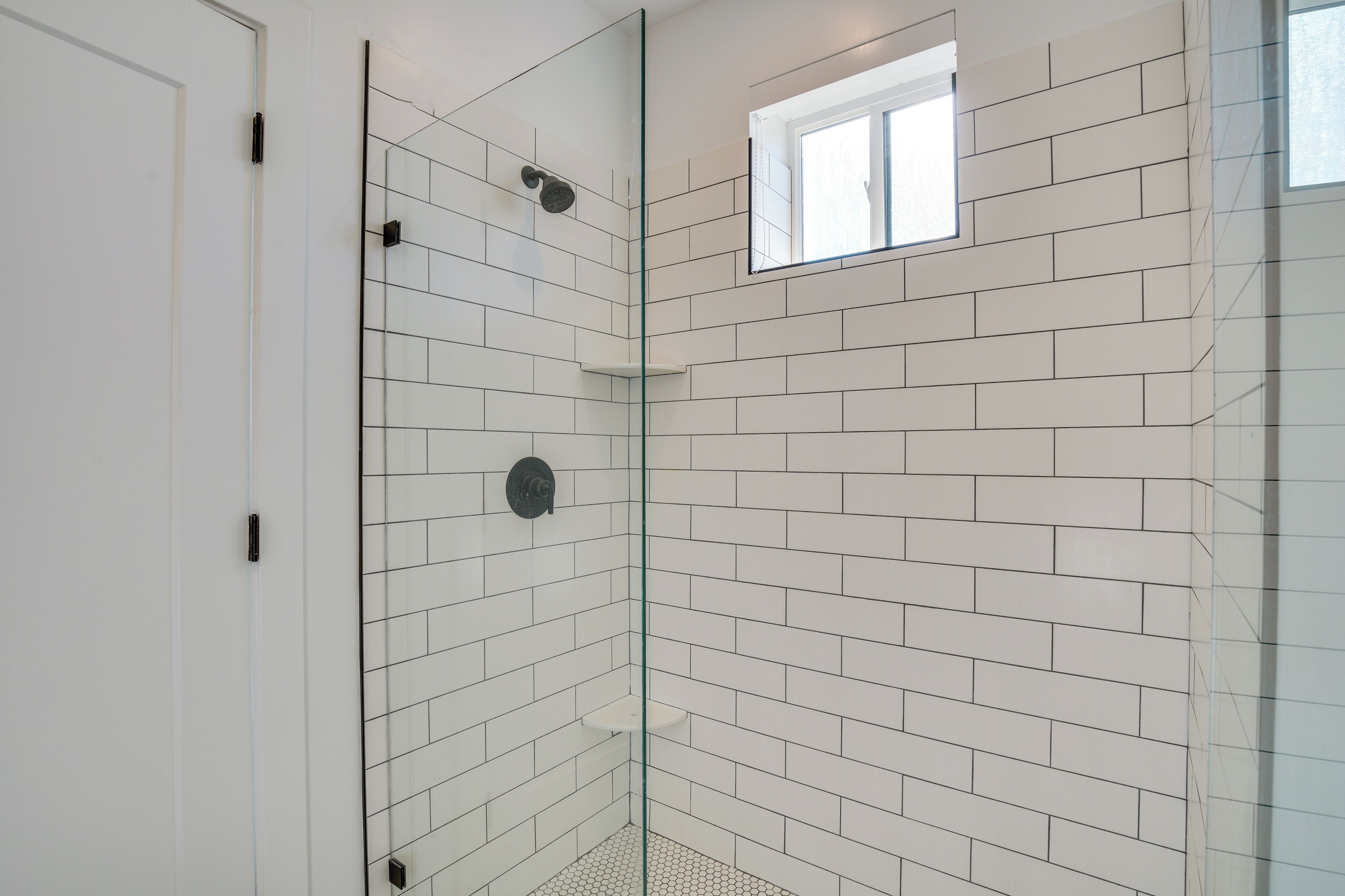 A modern bathroom with white subway tiles, a glass shower enclosure, and a small window.
