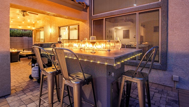 An outdoor bar area with a fire feature, bar stools, and a view of the interior through a window. - Gold Canyon Superstition Foothills Retreat w/ Pool (Gold Canyon)