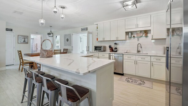 Una cocina moderna con armarios blancos, una isla central con taburetes, electrodomésticos de acero inoxidable e iluminación colgante.