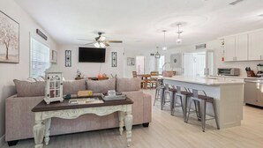 Una sala de estar moderna con un sofá, una mesa de centro y una zona de cocina con barra y taburetes.