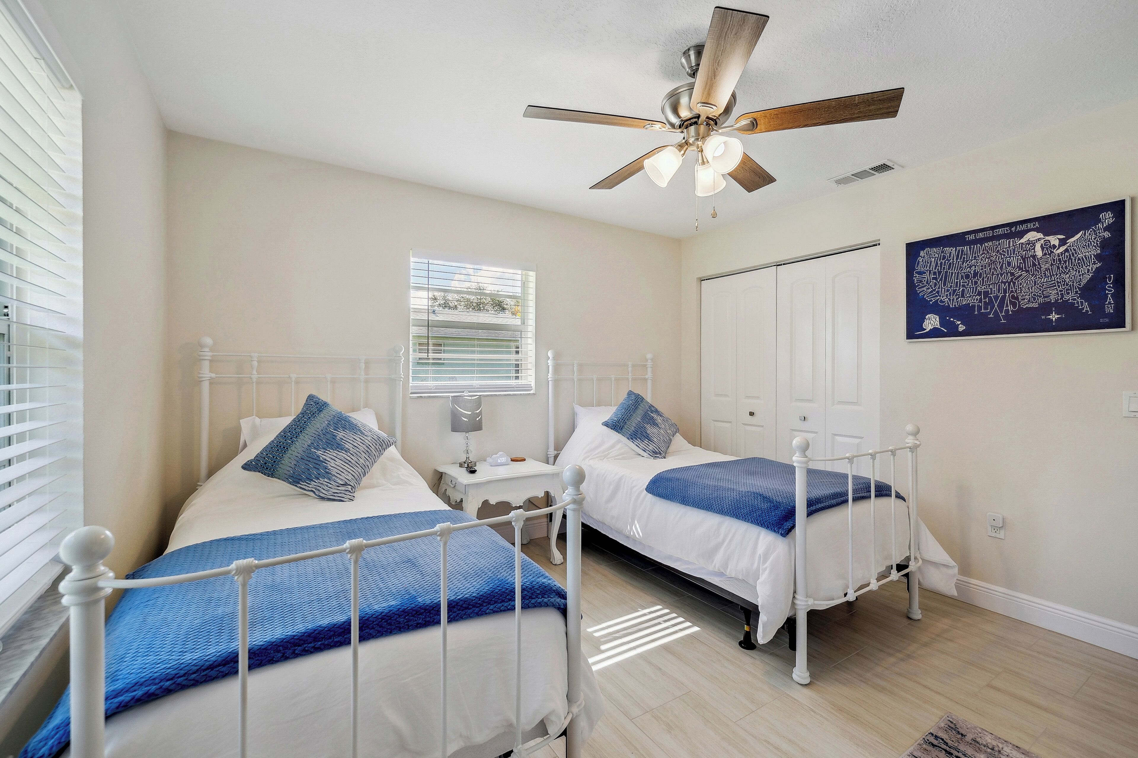 A bedroom with two beds, a ceiling fan, a window, and a map on the wall.