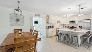 Una cocina moderna con armarios blancos, electrodomésticos de acero inoxidable y una isla central con taburetes de bar.
