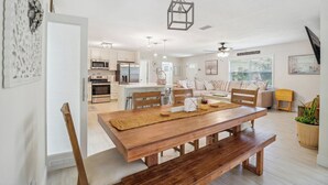 Una cocina moderna con armarios blancos, una isla central y un comedor con mesa de madera y bancos.