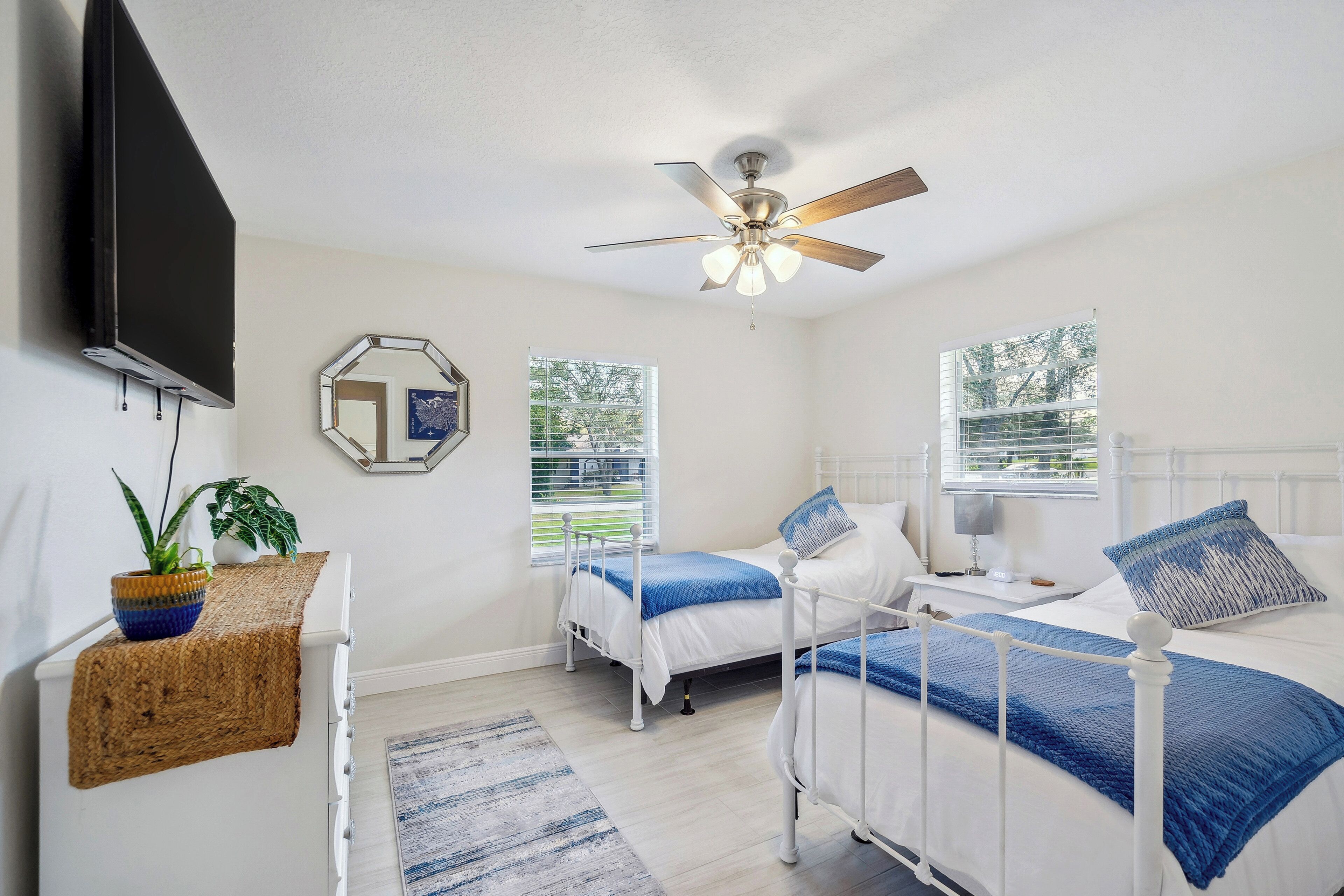 A bedroom with two beds, a ceiling fan, a TV, and a window with blinds.