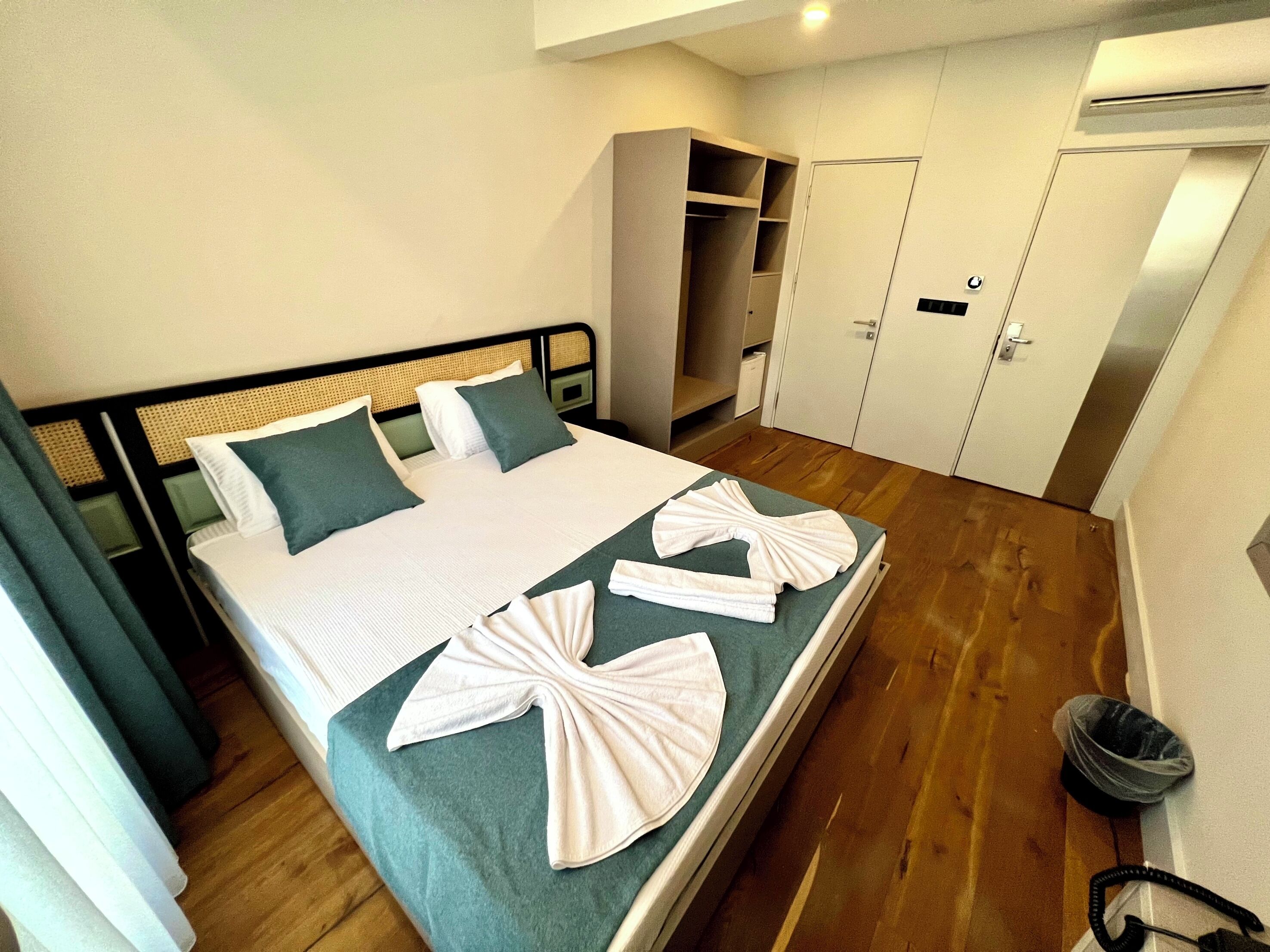 A neatly made bed with towels, a wardrobe, and a trash bin in a hotel room.
