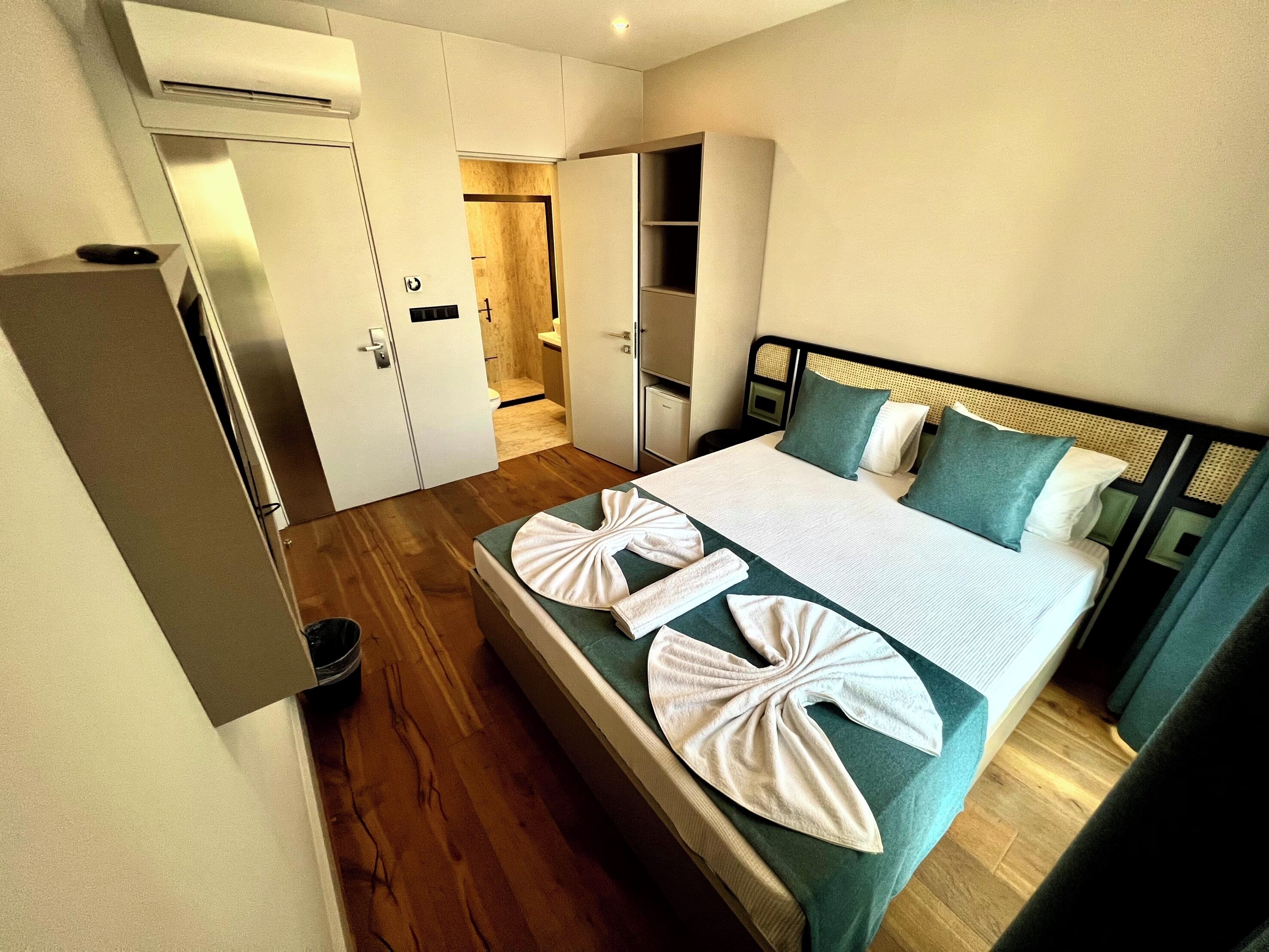 A hotel room with a large bed, a wardrobe, a bathroom, and a small desk.
