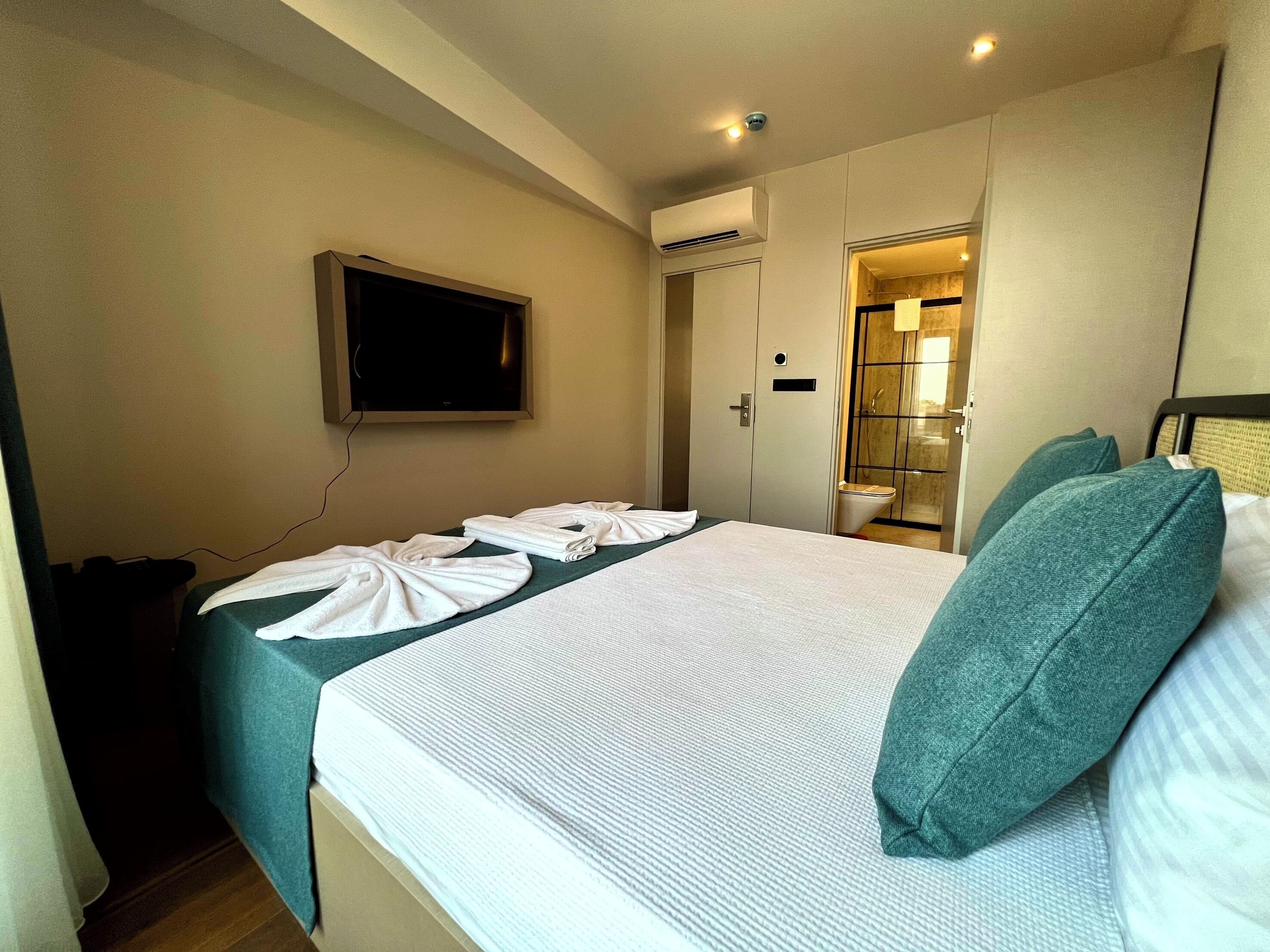 Habitación de hotel con cama, televisor montado en la pared y baño visible a través de una puerta abierta.
