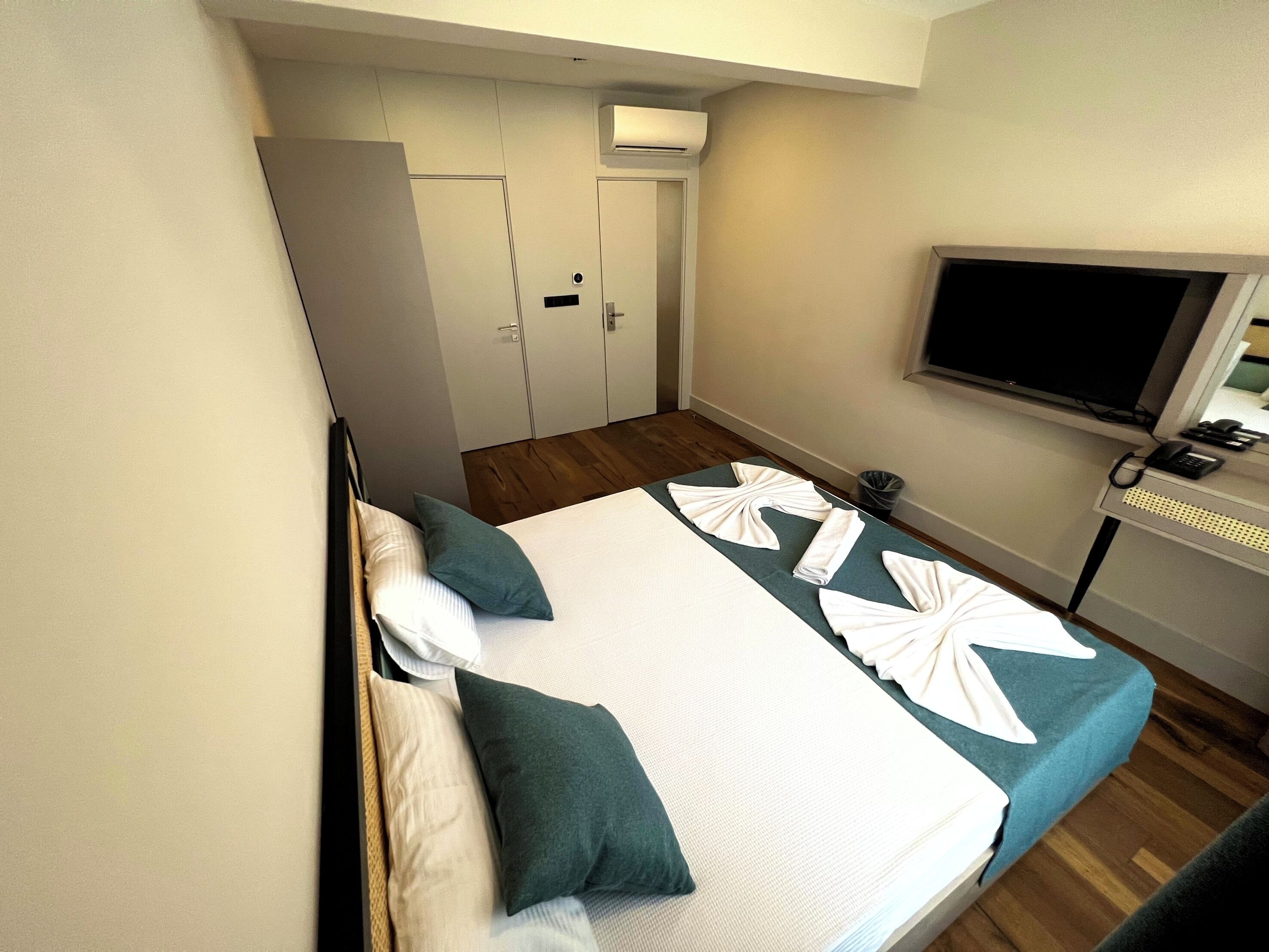 A hotel room with a bed, pillows, a TV, a desk with a phone, and a trash bin.
