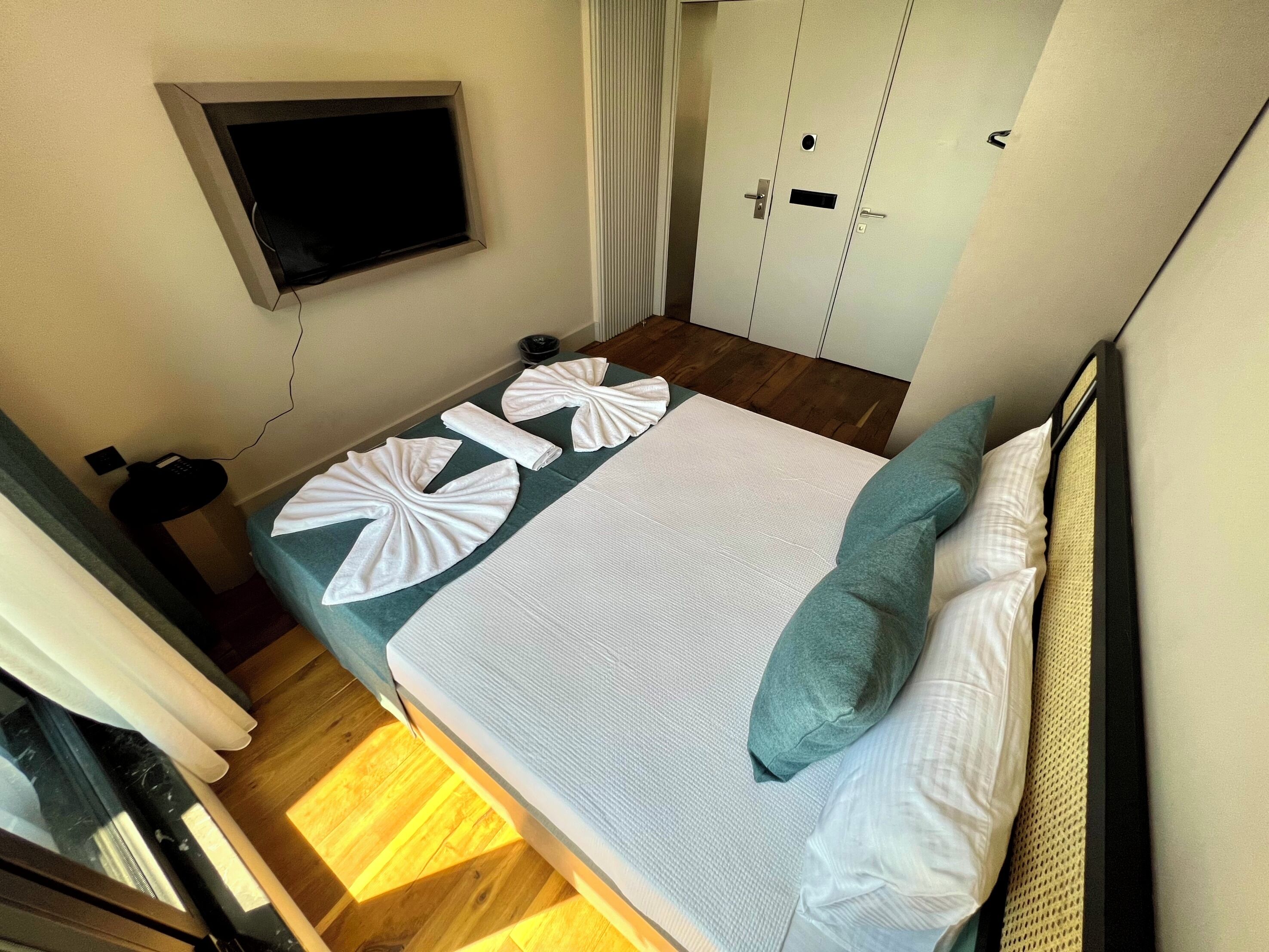 A hotel room with a bed, a TV mounted on the wall, and a wardrobe.