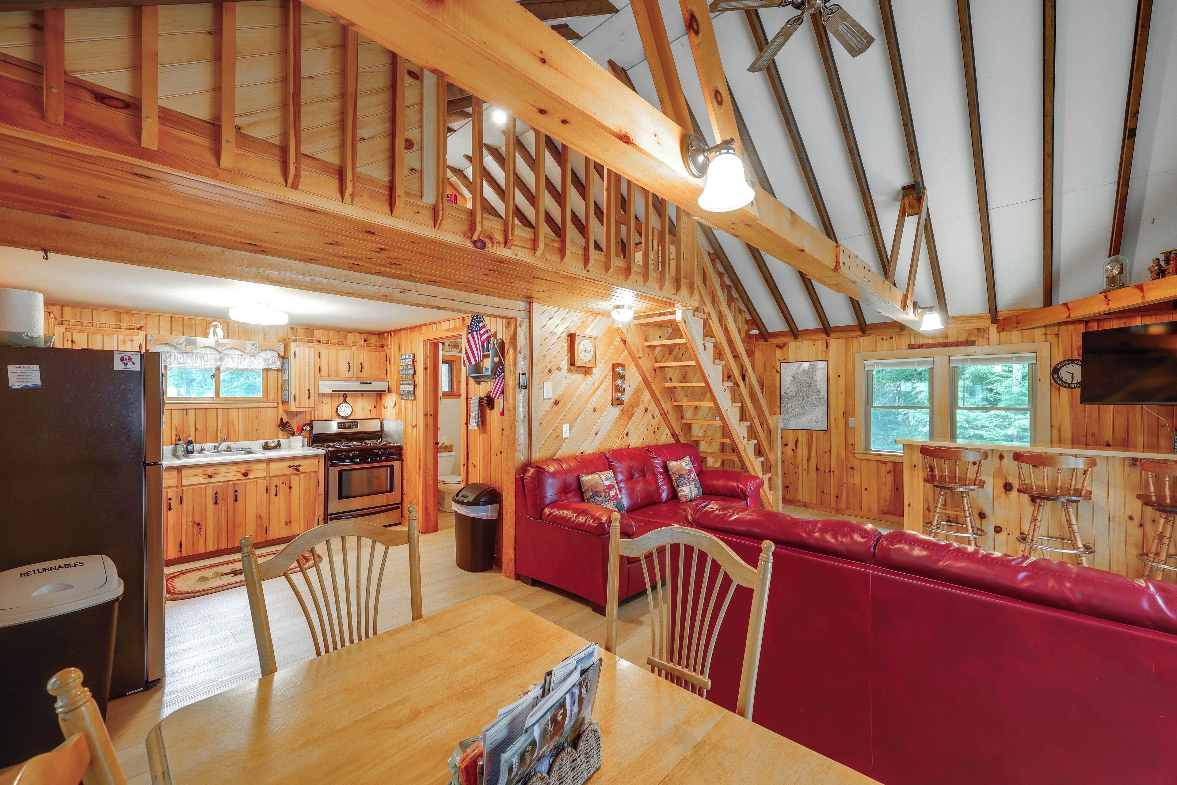 Interior de una cabaña de madera con cocina, comedor y un sofá de cuero rojo.