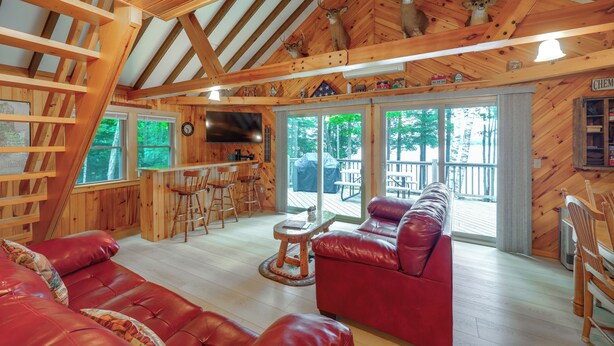 L’intérieur d’un chalet en bois est aménagé avec un canapé en cuir rouge, une table à manger en bois et un téléviseur fixé au mur.