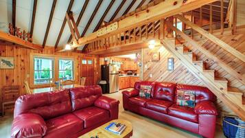 A log cabin interior with a red leather sofa, wooden staircase, and a kitchen area.