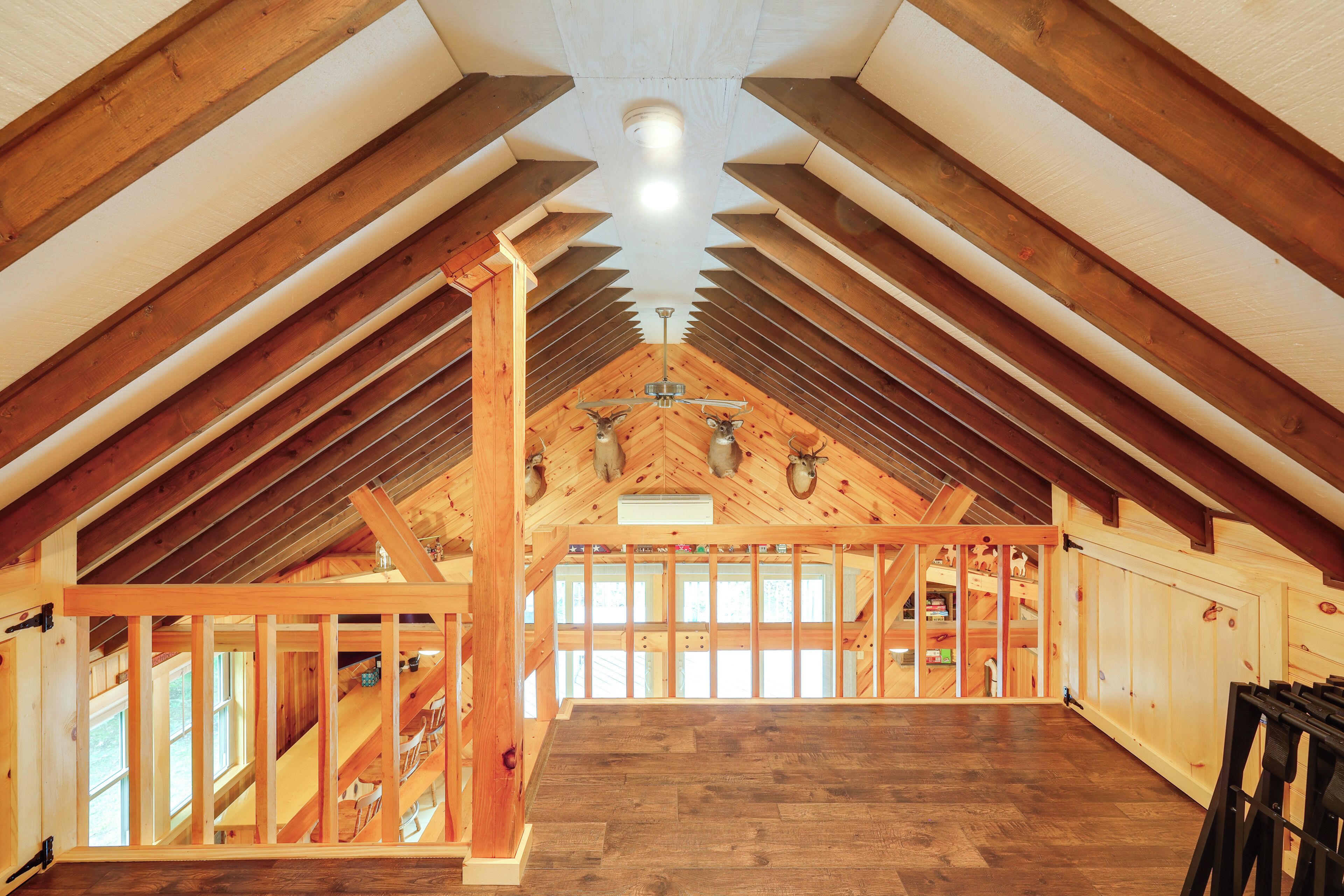 Amplia habitación en ático con vigas de madera, techo inclinado y un gran ventanal.