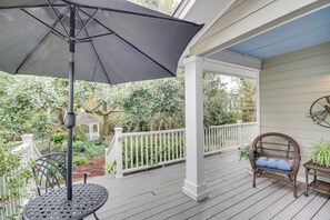 A covered porch with a table and chair, a black umbrella, and a garden view. - Ocean Springs Studio: Walk to Downtown & Beach! (Ocean Springs)