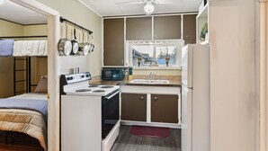A compact kitchen with a stove, microwave, and sink. A bunk bed is visible in the adjacent room. - Choteau Vacation Rental w/ Yard: Walk to Downtown! (Choteau)