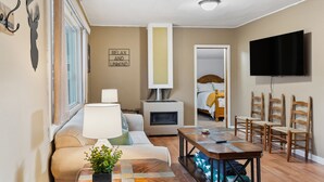 A modern hotel room with a sofa, a table, a fireplace, a TV, and a bed in the background. - Choteau Vacation Rental w/ Yard: Walk to Downtown! (Choteau)
