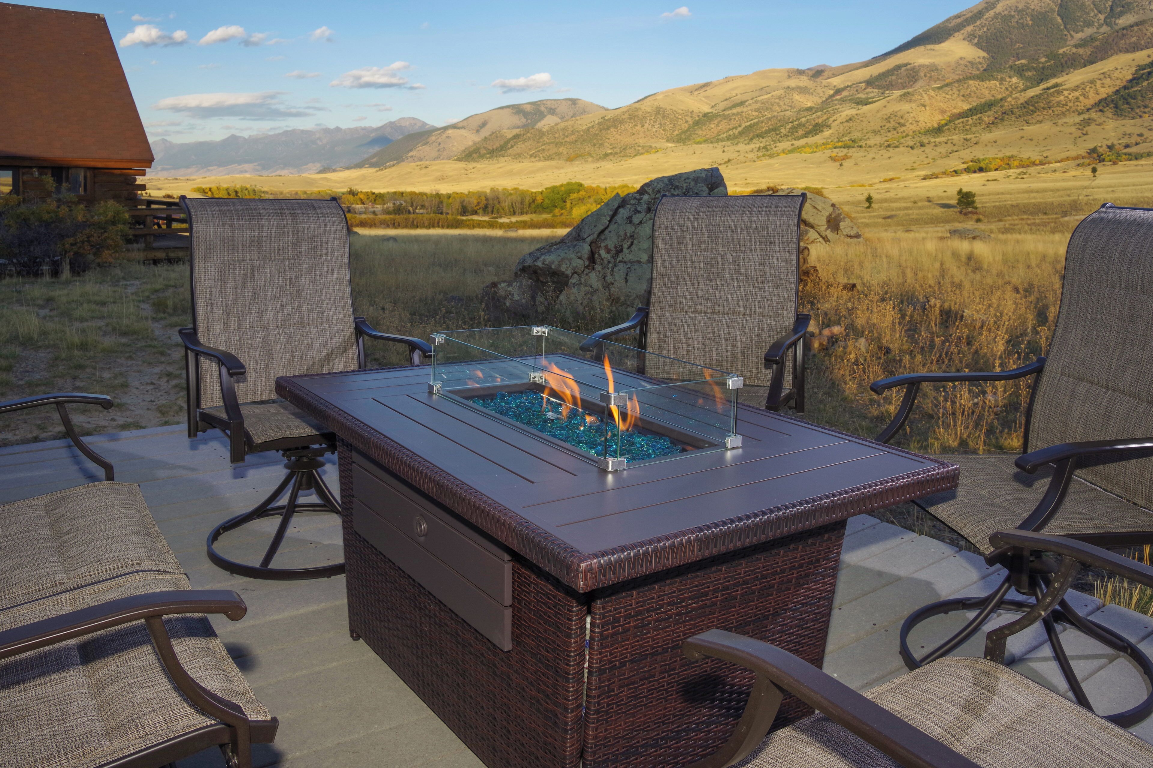 A patio with a fire feature, wicker chairs, and a view of mountains.
