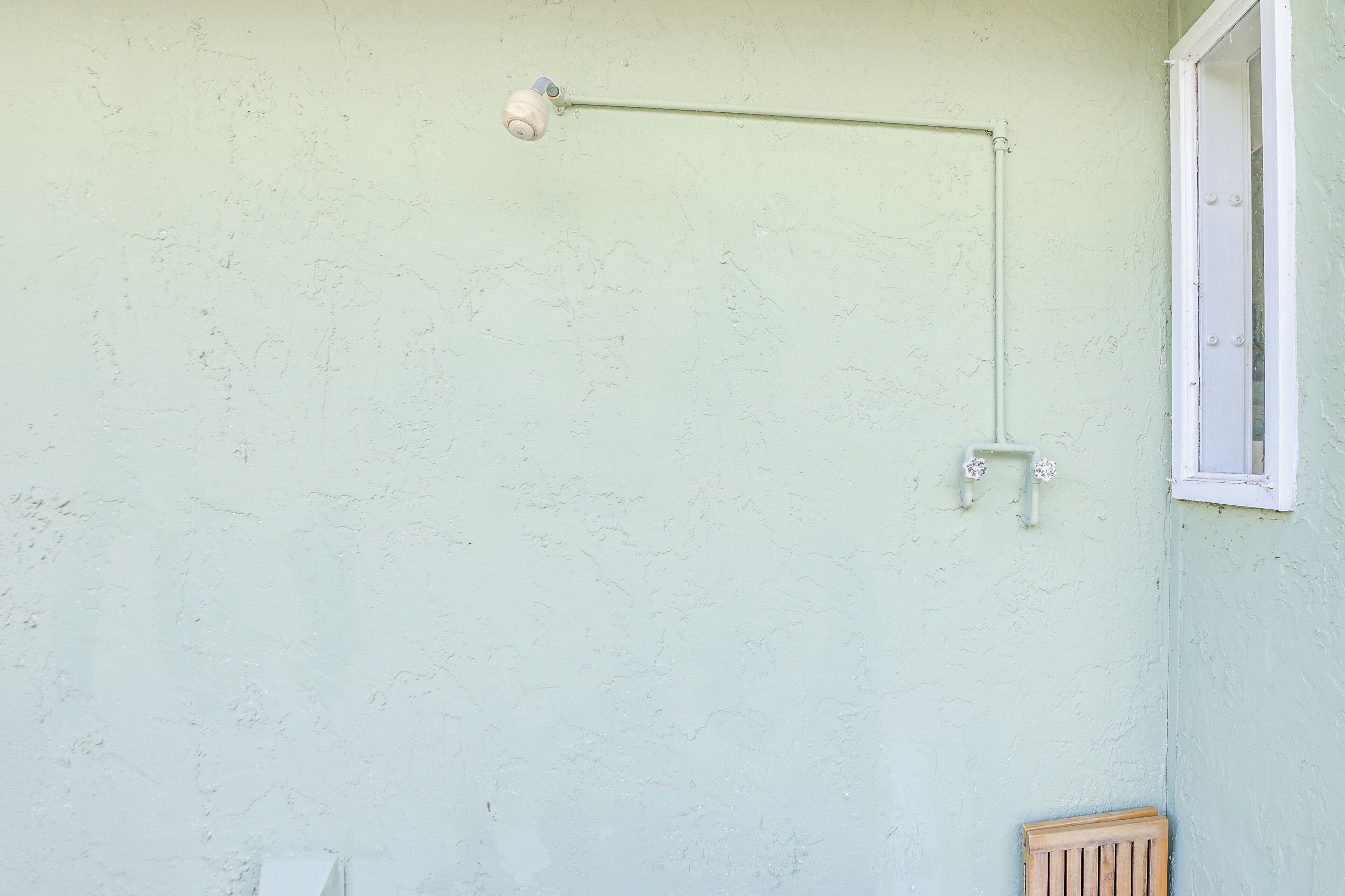 A room with a light green wall, a window with white trim, and a wooden bench.