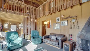 A spacious living area with a high ceiling, wooden beams, a fireplace, and a cozy seating arrangement. - Red Feather Lakes Cabin w/ Deck & Views! (Red Feather Lakes)