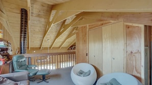 A wooden interior with a high ceiling, a balcony with a railing, a green leather chair, a white bean bag chair, and a sofa. - Red Feather Lakes Cabin w/ Deck & Views! (Red Feather Lakes)